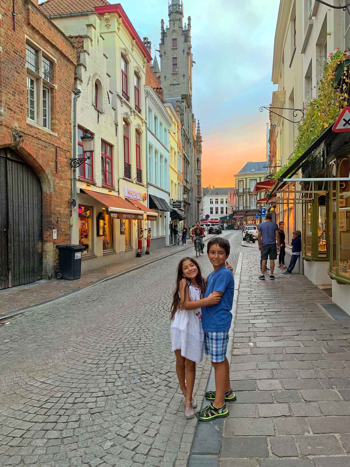 A brother and sister embrace on a historic street in Bruges, while exploring Belgium as a family.