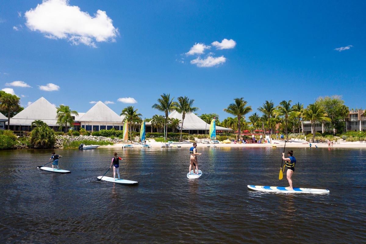 Four people float along the water on stand-up paddle boards, while staying at Club Med Sandpiper Bay, one of the best all-inclusive hotels in the United States for families.