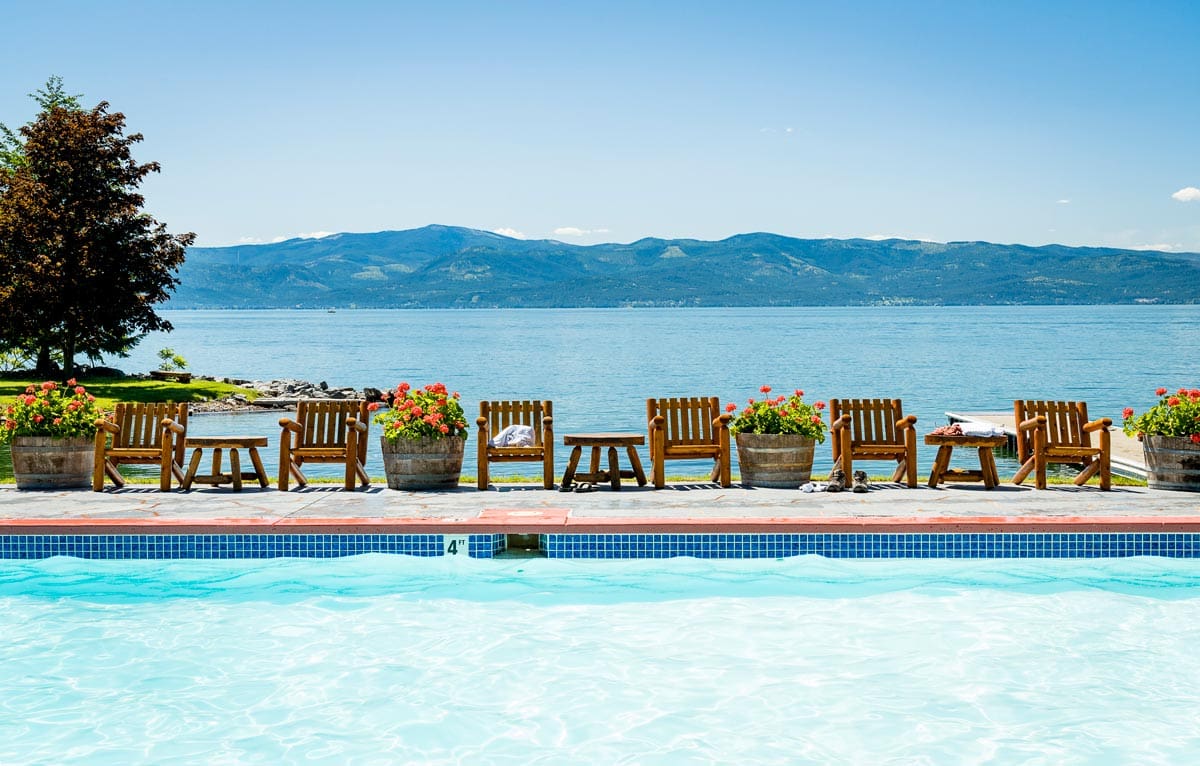 A line of deck chairs face the pool, with a lake in the distance, at Flathead Lake Lodge.