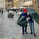 Two kids walk along a street in Florence with umbrellas on a rainy day.