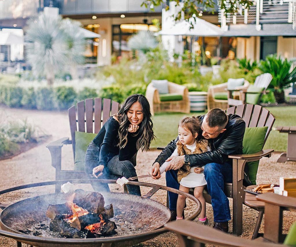 A family of three roasts marshmallows over a fire pit, while staying at Four Seasons Hotel Austin, one of the best hotels in Austin for families.