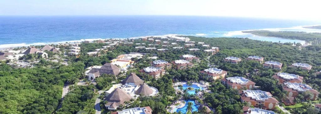 An aerial view of the resort buildings and grounds of Grand Bahia Principe Coba, nestled along the ocean.