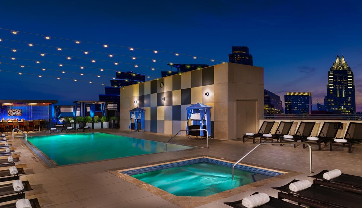 The outdoor pool and hot tub, surrounded by a spacious pool deck at night at Hilton Austin.