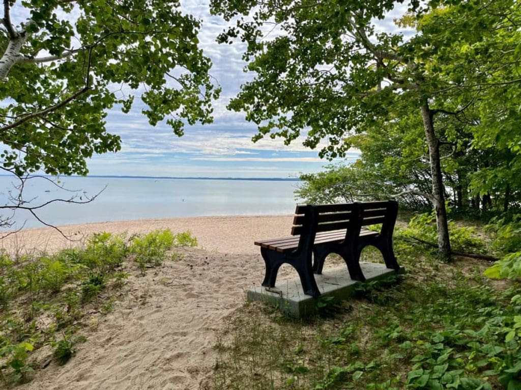 An empty bench rests along a beach with a view of the lake at Mission Point Park in Traverse City, Michigan, one of the best places to visit in Michigan with kids.