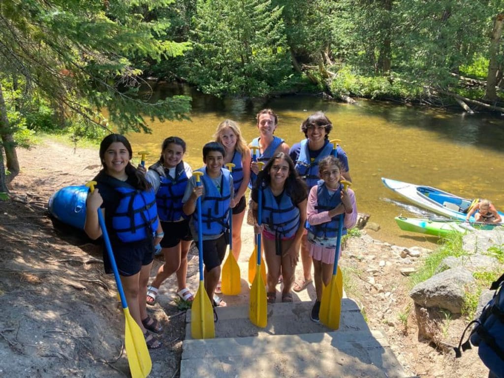 A group of teens, wearing life jackets and holding paddles, awaits a rafting trip down the Indian River in Michigan.
