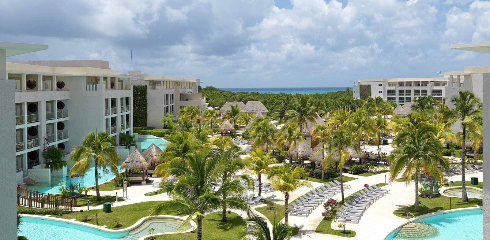 An aerial view of the hotel buildings and grounds at Paradisus Playa del Carmen, featuring several pools and many palm trees.