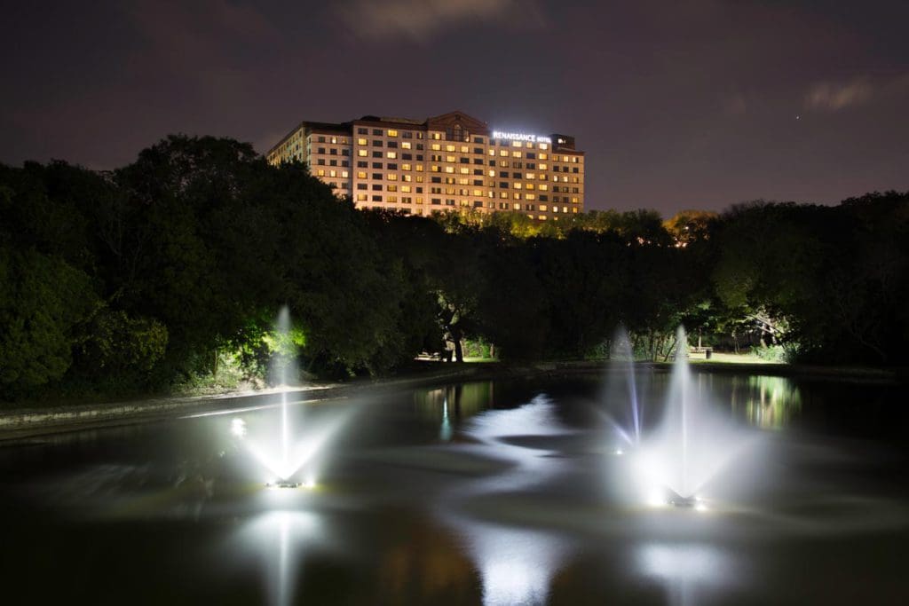 The hotel building of The Renaissance Austin Hotel peaking through the trees, behind a large water feature.