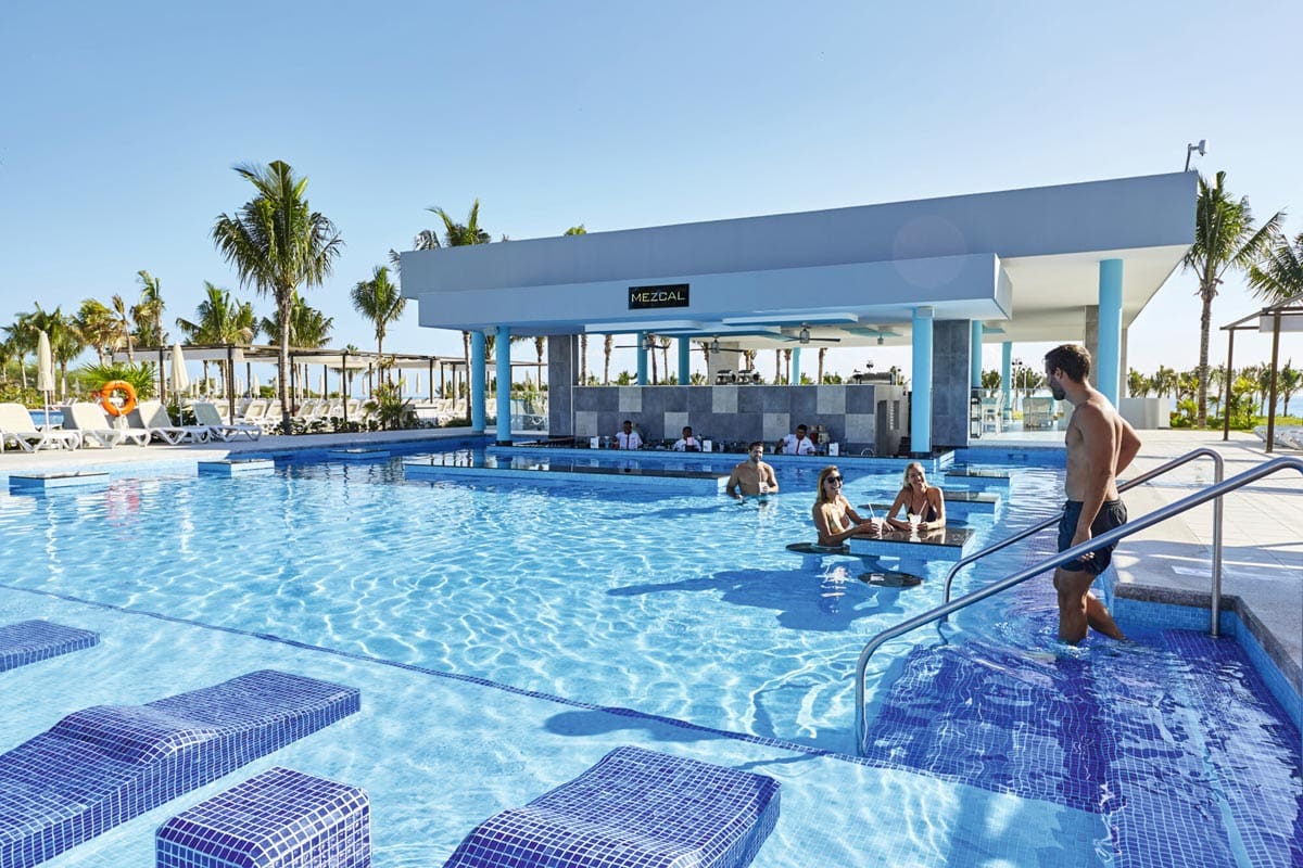 Several adults swim and sit at the swim-up bar in a pool at Riu Dunamar, one of the best resorts in Mexico with a water park for families.