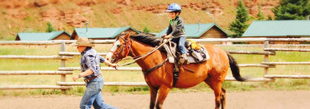 A staff member at Red Rock Ranch leads a horse carrying a small boy within a horse pen.