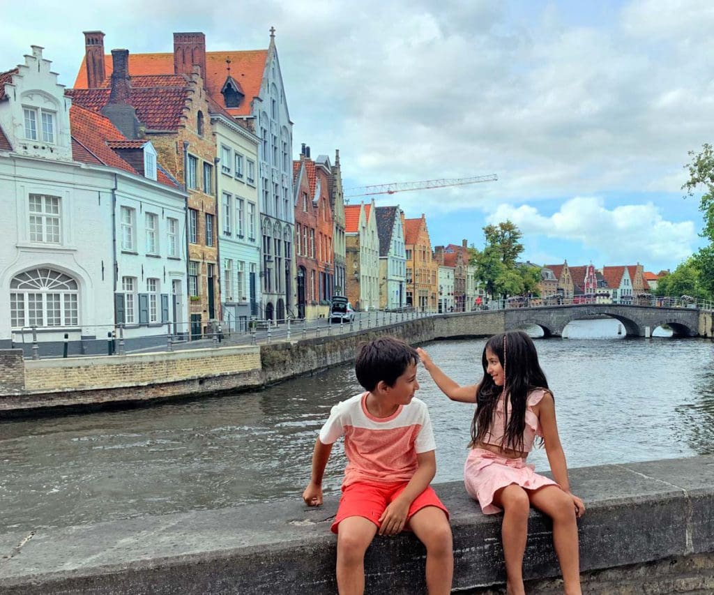 Two kids sit together on the wall of a canal in Bruges.