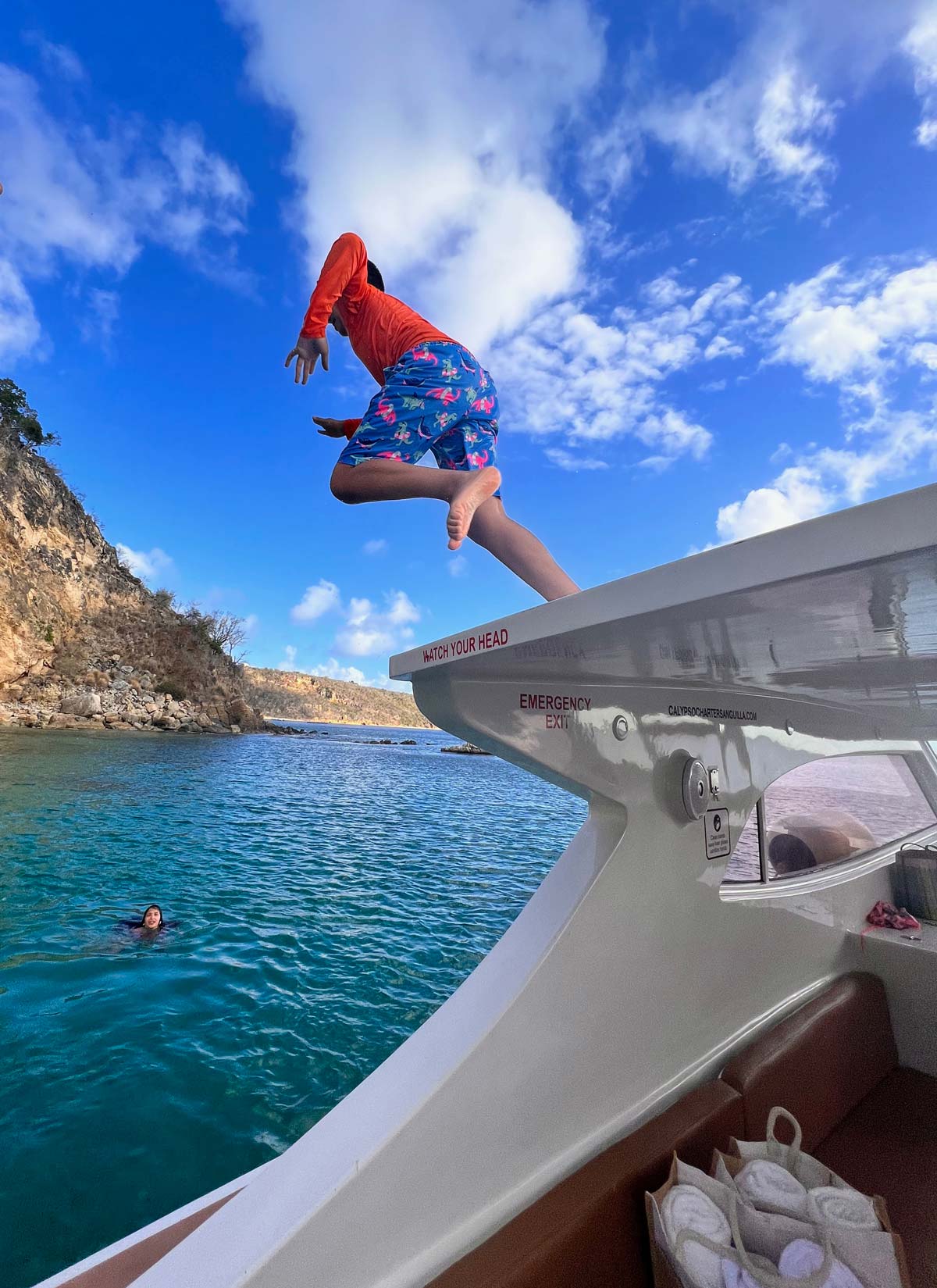 A young boy jumps from a boat into the Caribbean ocean.