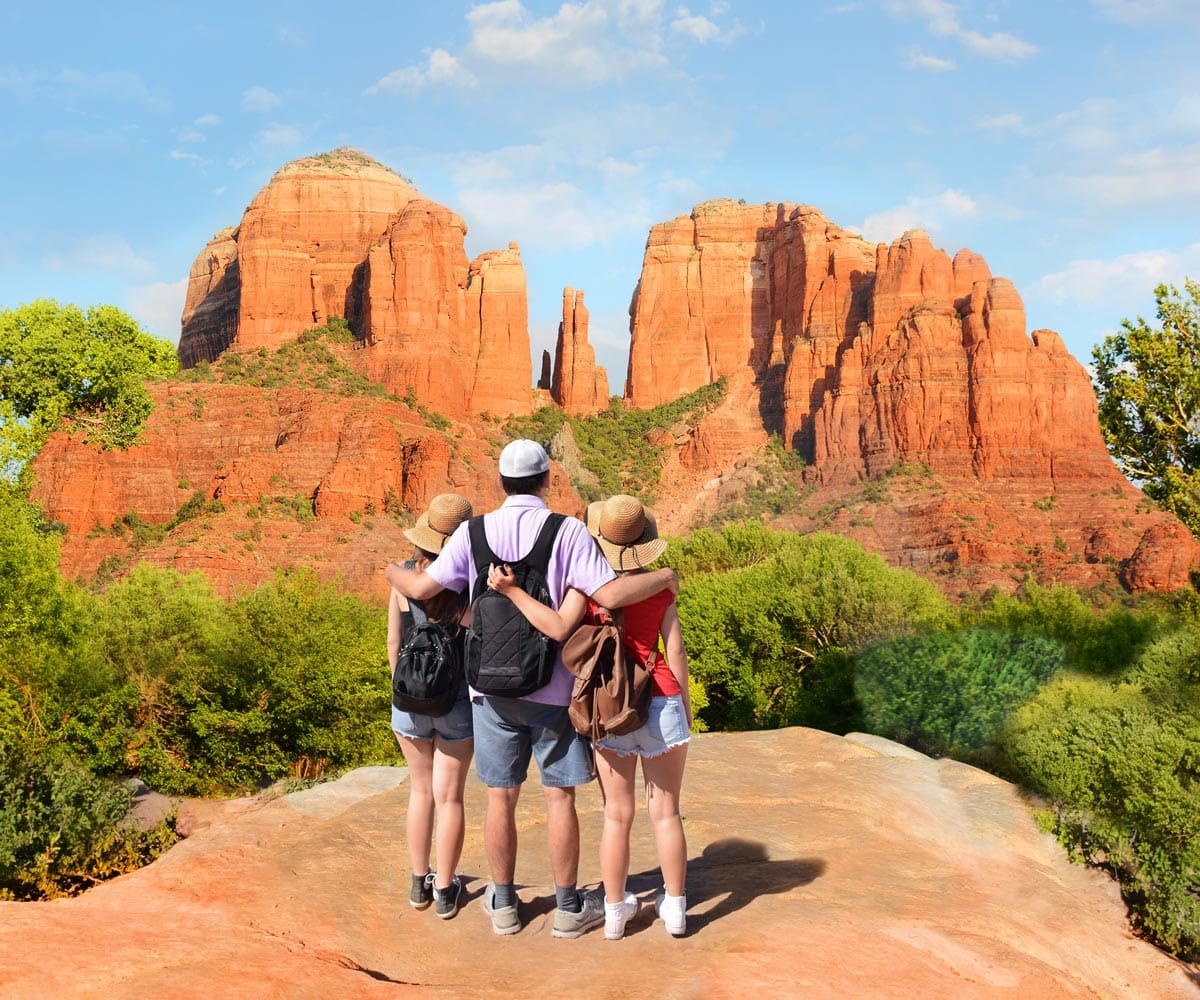 A family of three stands together enjoying a view of Sedona's iconic red rock formations on a sunny day.