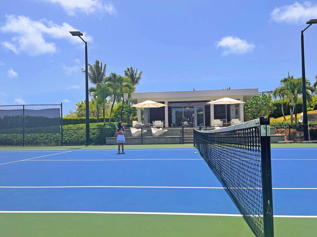 A young girl awaits her turn in tennis on the on-site court at Four Seasons Resort and Residences Anguilla.