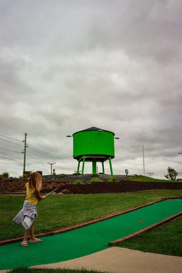 A young girl swings a mini golf club at a ball on the green at Action City.