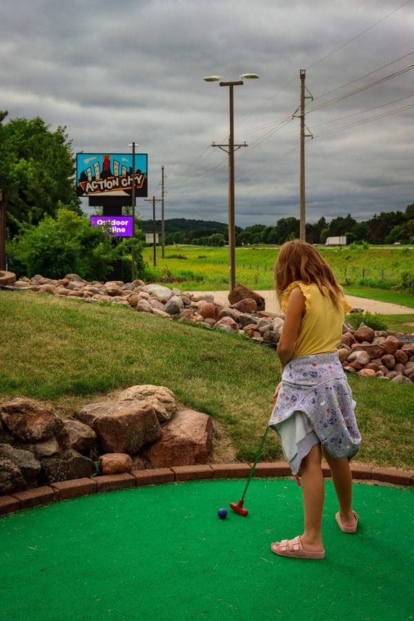 A young girl squares up to hit a mini golf ball at Action City, one of the best things to do in Eau Claire with kids.