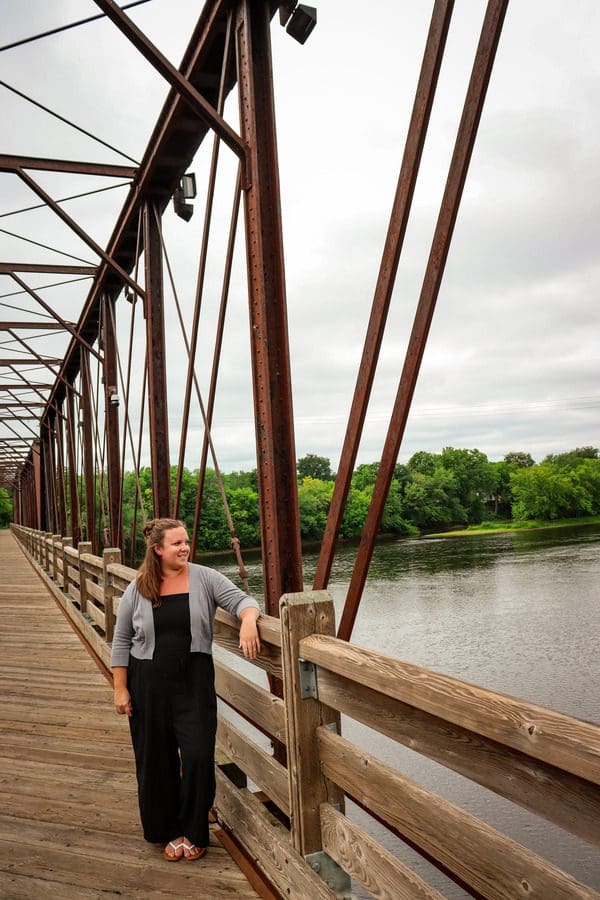 A woman leans against the edge of a bridge, admiring the river below.