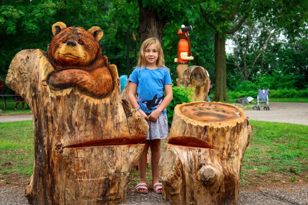 A young girl stands behind a large chainsaw wood carving of a bear at the US Open Chainsaw Sculpture Championship, one of the best seasonal things to do in Eau Claire with kids.