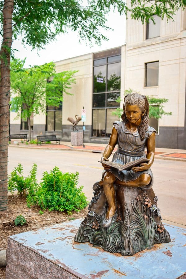 A statue of a young girl reading a book on a street in Eau Claire, as part of the Eau Claire Sculpture Tour, one of the best things to do in Eau Claire with kids.
