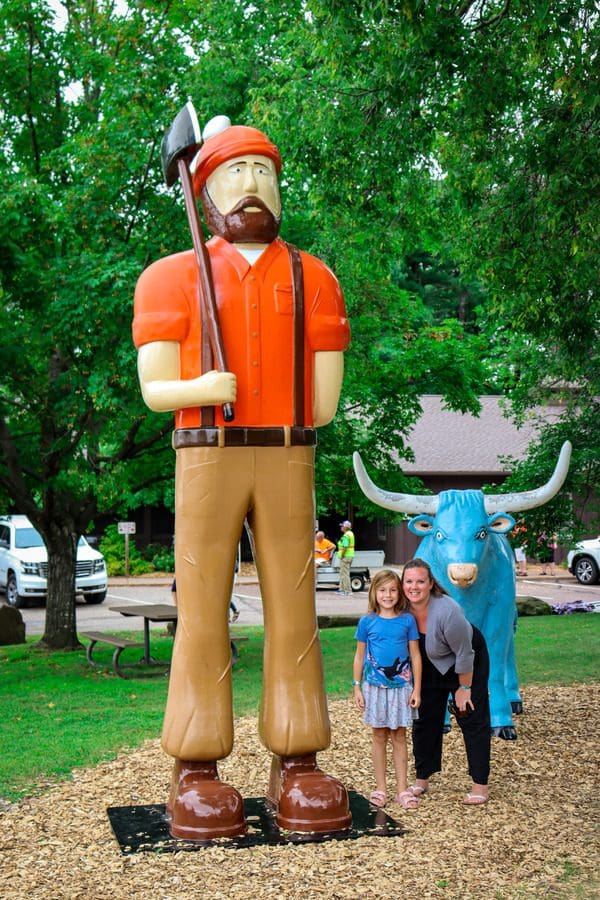A young girl and her mom stand near huge statues of Paul Bunyan and Babe the Blue Ox in Carson Park, one of the best things to do in Eau Claire with kids.