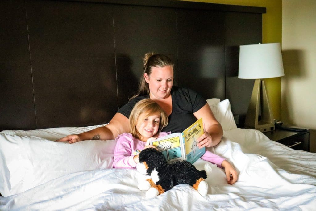 A mom and her young daughter read a book together, while snuggled up in bed at the Staybridge Suites in Eau Claire.