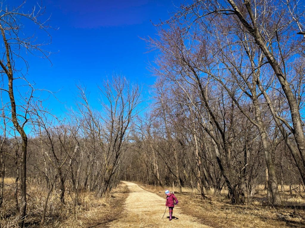 A young girl walks down a hiking path at Minnesota Valley National Wildlife Refuge in the spring in Bloomington, one of the best places to visit with your young daughter in America.