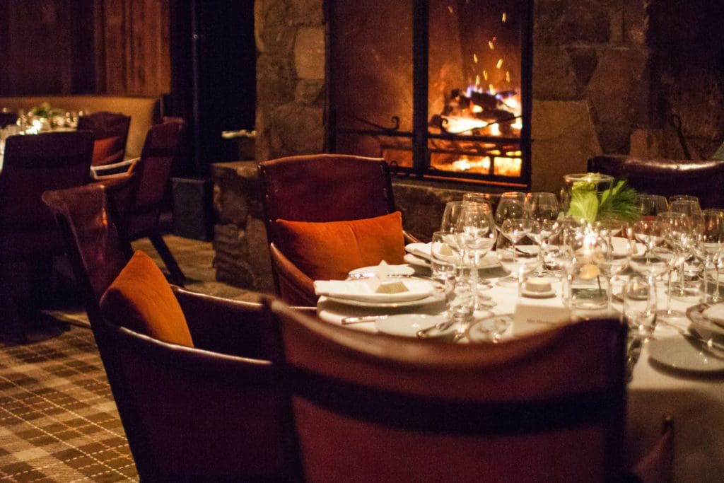 A table set for dinner near a cozy fire at The Barn, and on-site dining location at Blackberry Farm.