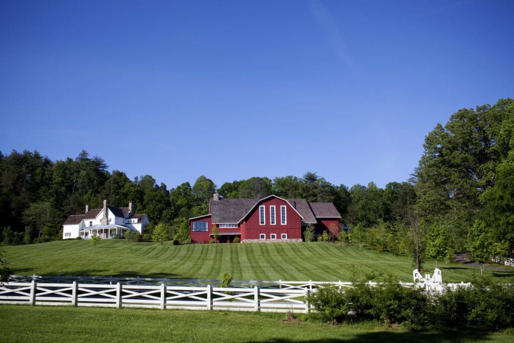 The iconic red barn at Blackberry Farm in Tennessee, surrounded by lush green fields and a white fence on a sunny day.