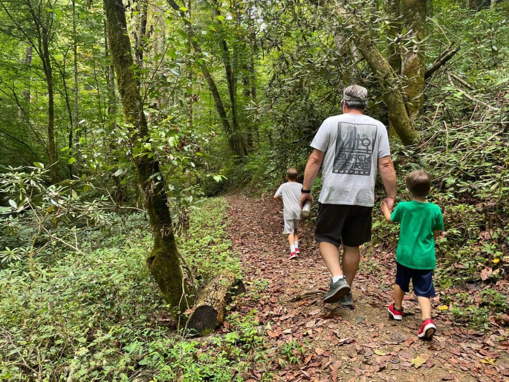 A dad and his two young sons walk along a wooded hiking path on-property, while on a family getaway to Blackberry Farm in Tennessee.
