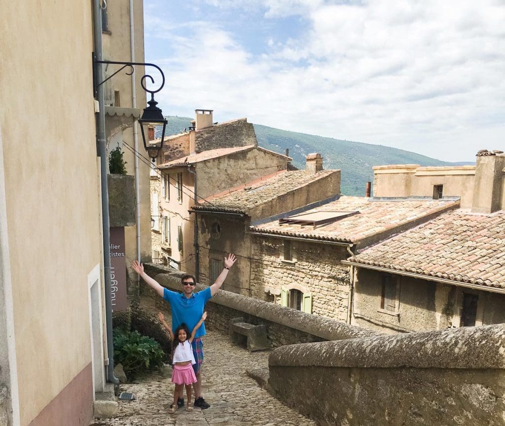 A young girl and her dad stand together with a rooftop view of Bonnieux behind them, one of the best towns in the South of France with kids.