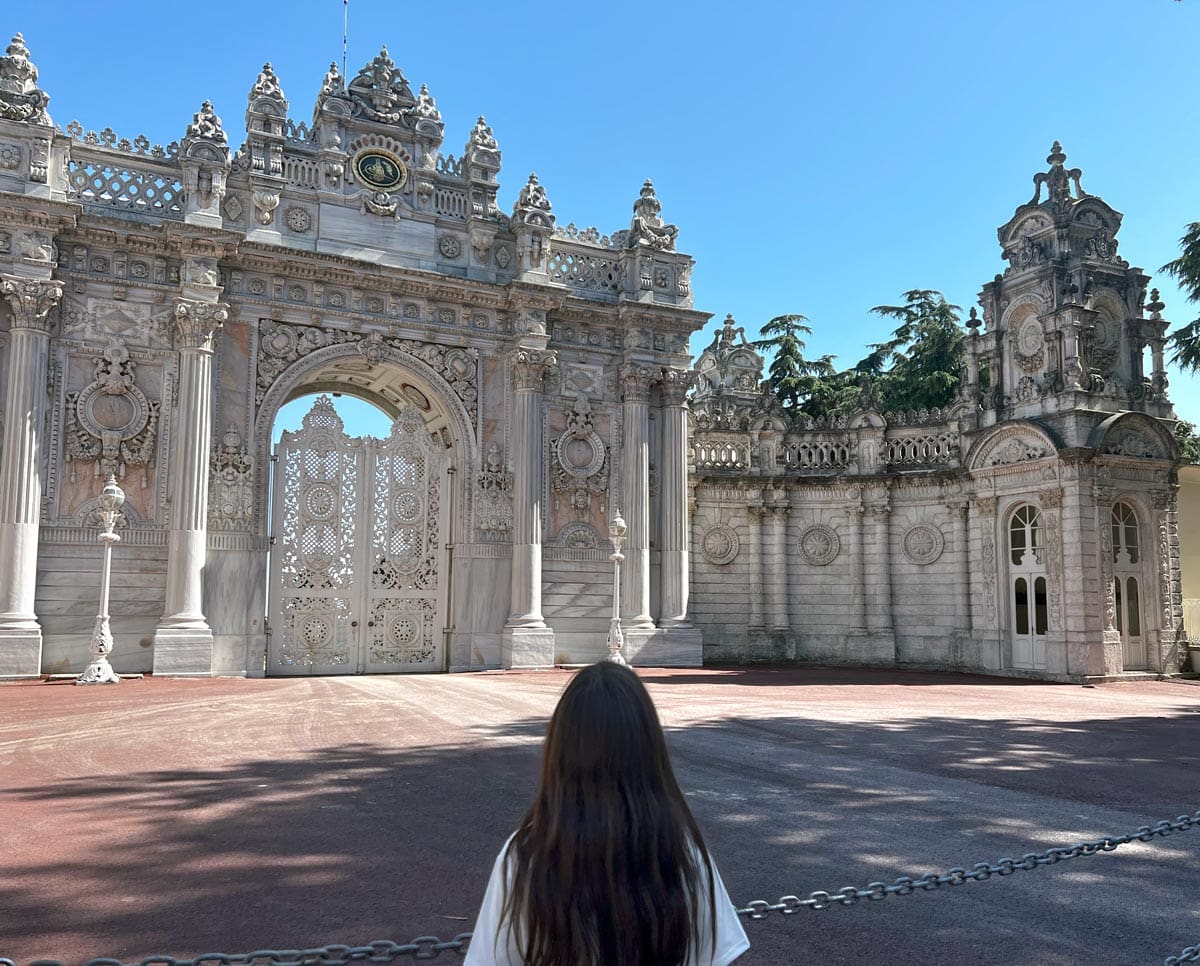 A young girl walks toward a grand arch on the grounds of Dolmabahçe Palace.