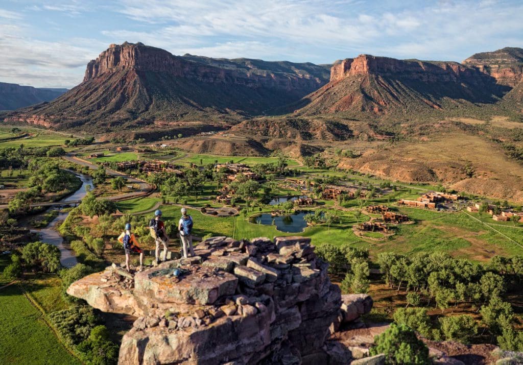 A dad and two teenagers stand atop a scenic hiking trail overlooking the sprawling property of Gateway Canyons Resort & Spa, one of the best eco-friendly hotels in the United States for families.