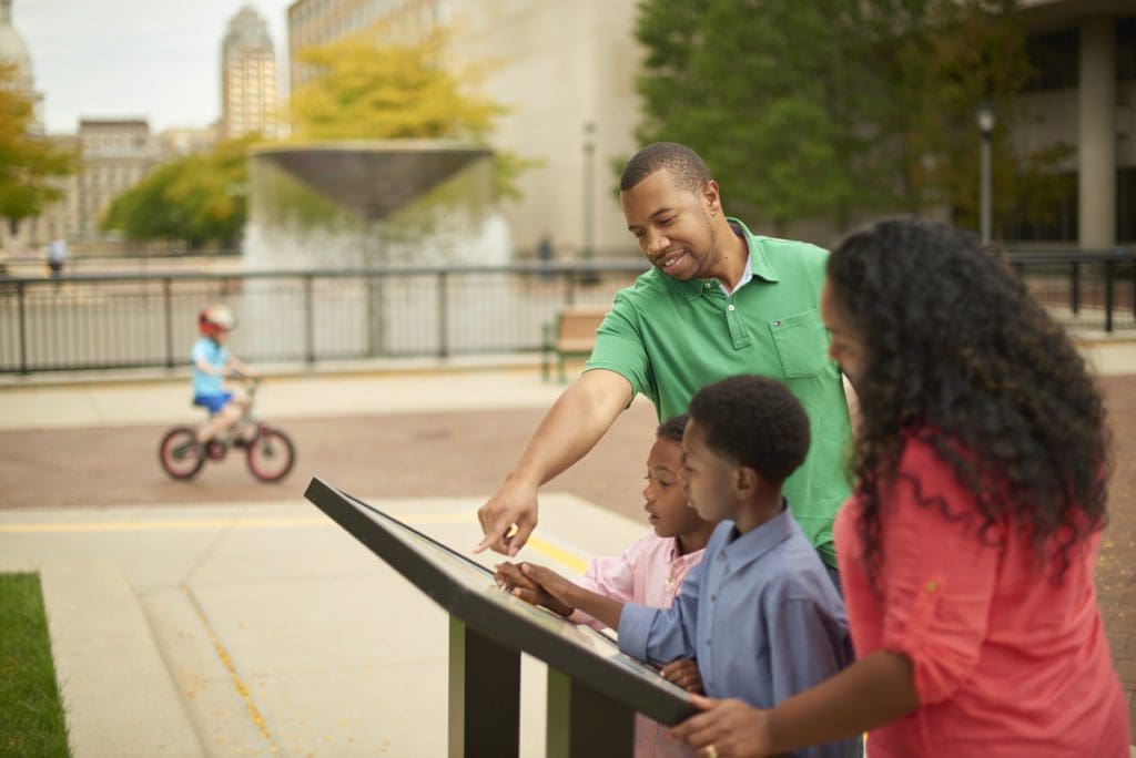 A family looks at an informational plaque while exploring Lansing together.