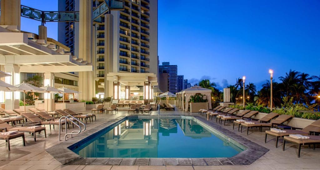 The cozy outdoor pool and surrounding pool deck near the towering resort buildings at Hyatt Regency Waikiki Beach Resort and Spa.