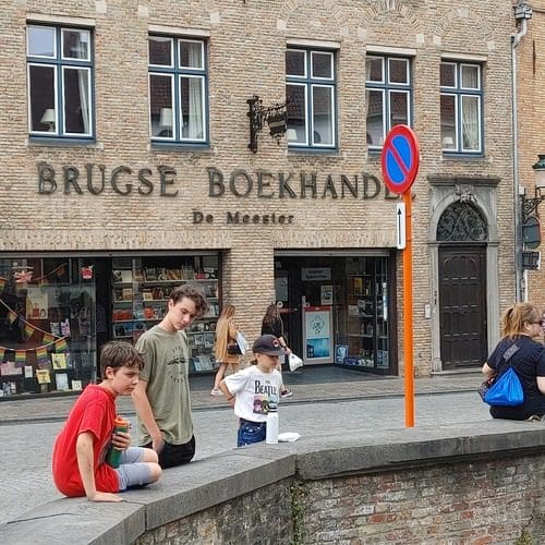 Three boys sit along a ledge, while exploring Bruges as a family.