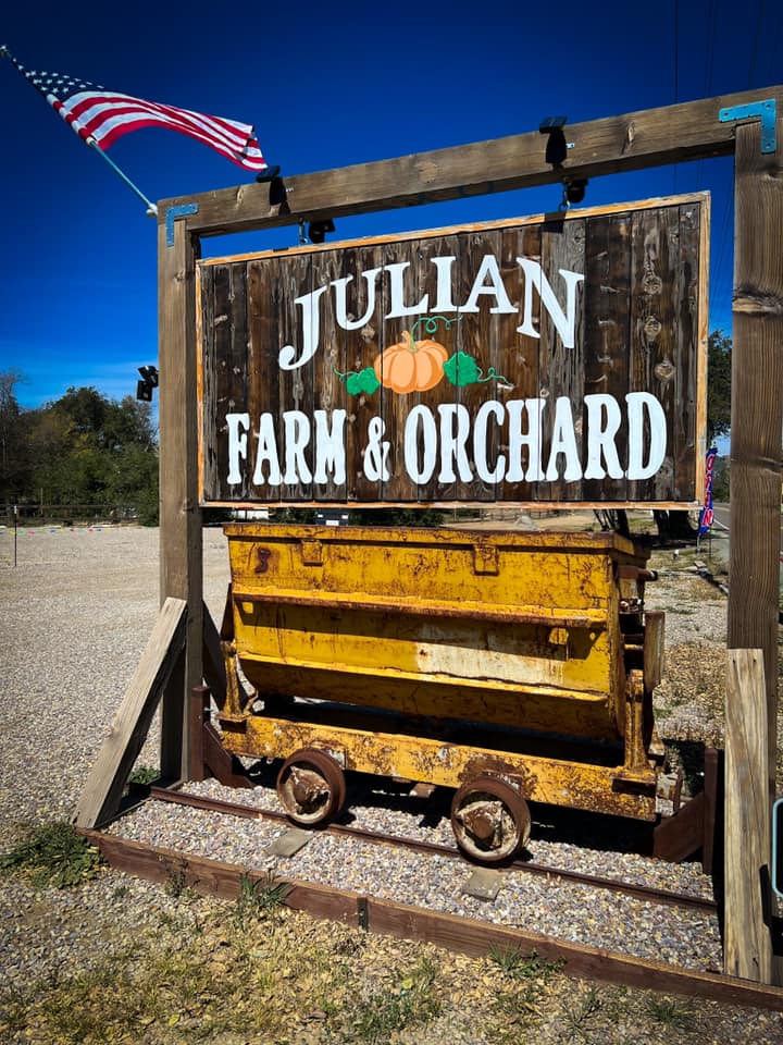 A close up of the entrance sign, waving an American flag, to Julian Farm and Orchard, one of the best places to visit in Julian with kids.