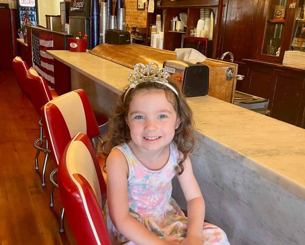 A young girl wearing a princess crown sits at a diner counter in Julian.