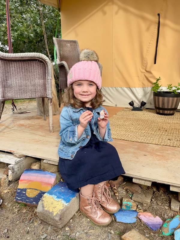 A young girl sits on the platform of a glamping tent, while visiting Julian, California as a family.