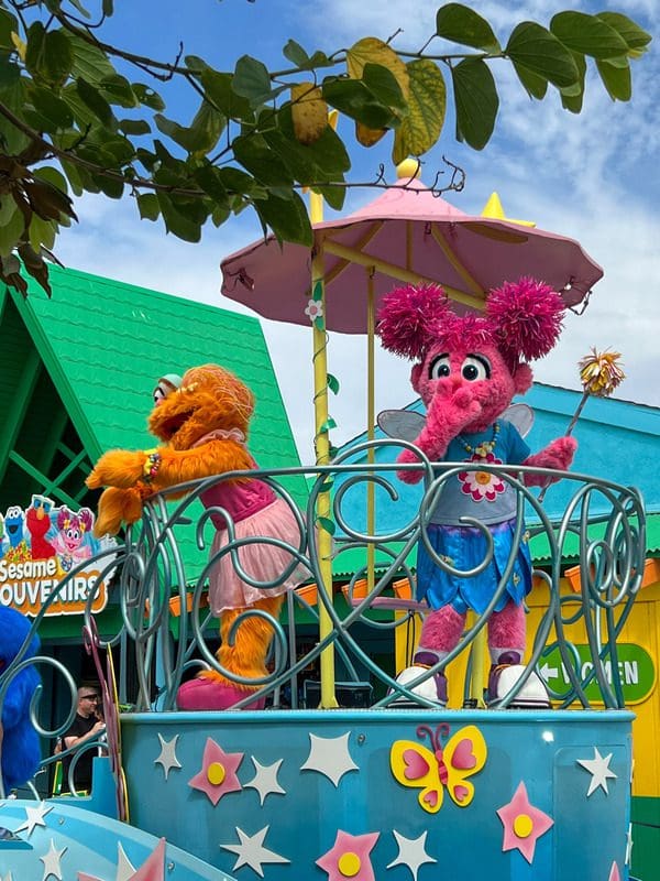 Two Sesame Street characters dance atop a parade float.
