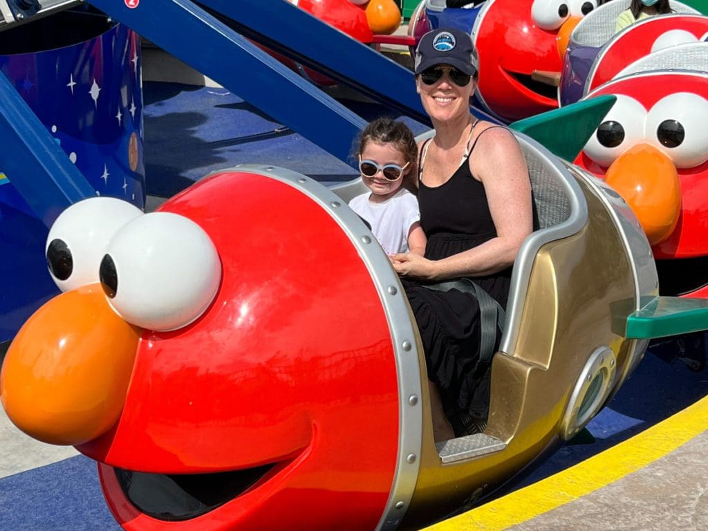 A mom and her young daughter ride together on an Elmo-themed ride at Sesame Place San Diego.