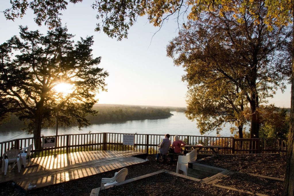 Two people sit on a patio along a lakeshore in Lake of the Ozarks, Missouri, enjoying the autumn scenery.