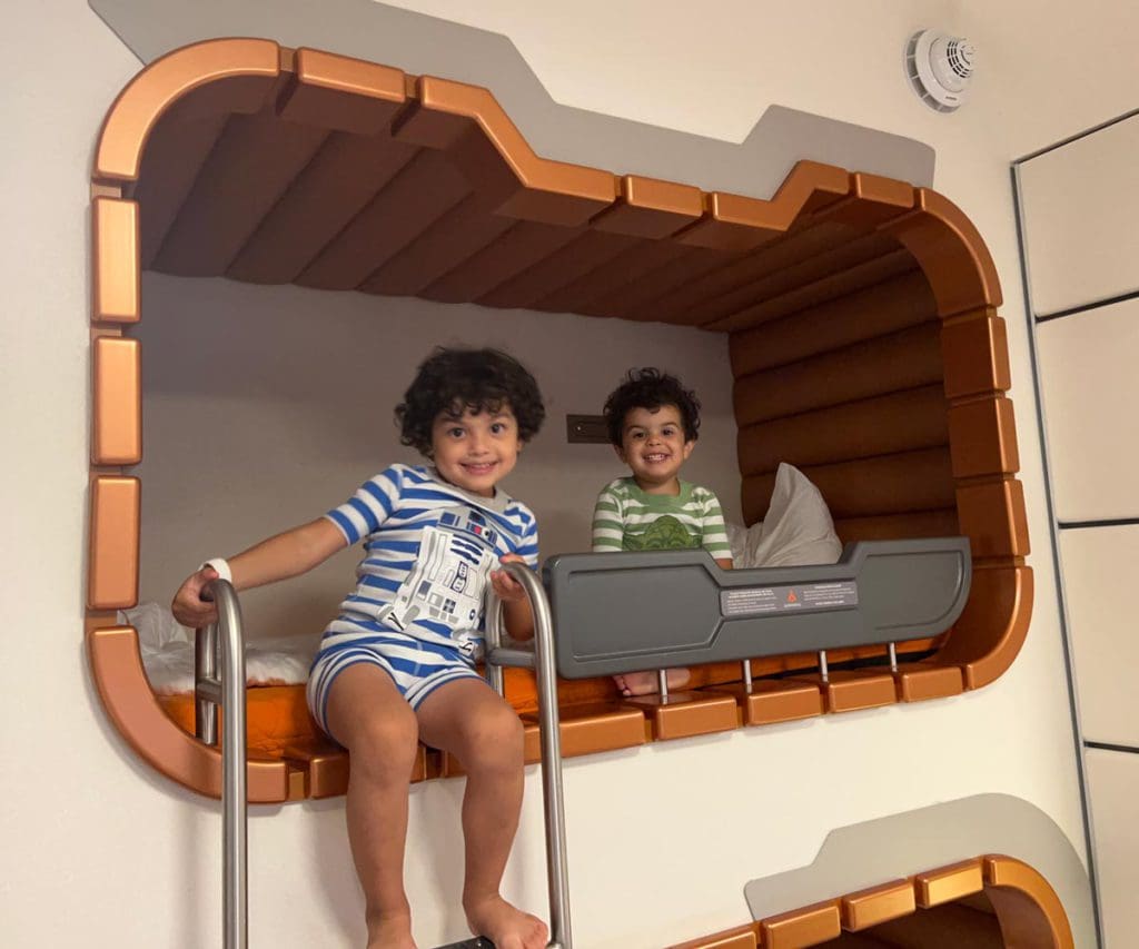 Two young boys sit on a bunk bed together, while staying at Star Wars Galactic Starcruiser.