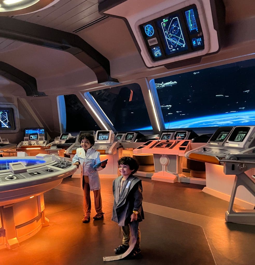 Two kids in costume stand in the bridge of the Star Wars Galactic Starcruiser, while receiving "Bridge Ops Training".