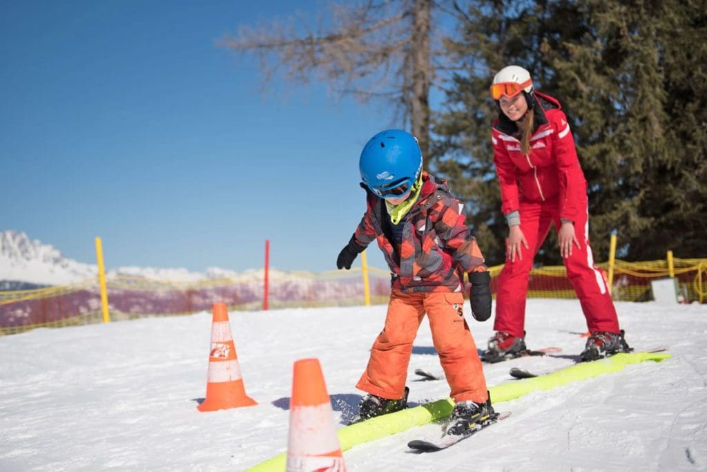 A young skier, followed by an instructor, makes their way through a ski lesson course at The Rot Weiss Rot Ski School.