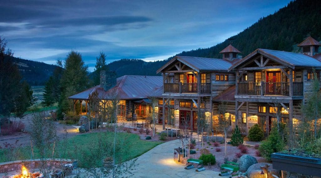 The back exterior of the main building at The Ranch at Rock Creek, featuring well-lit balconies for guest at night and the mountains in the distance.
