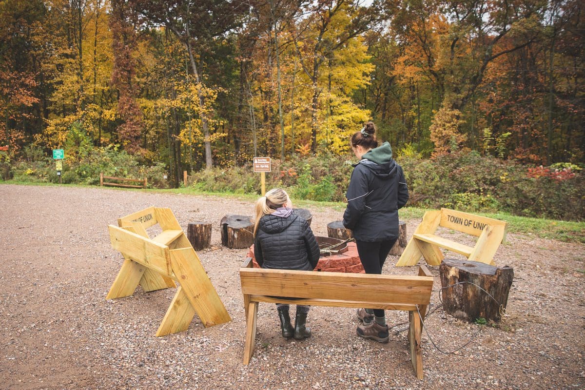 Two women sit around a fire pit on a crisp fall afternoon.