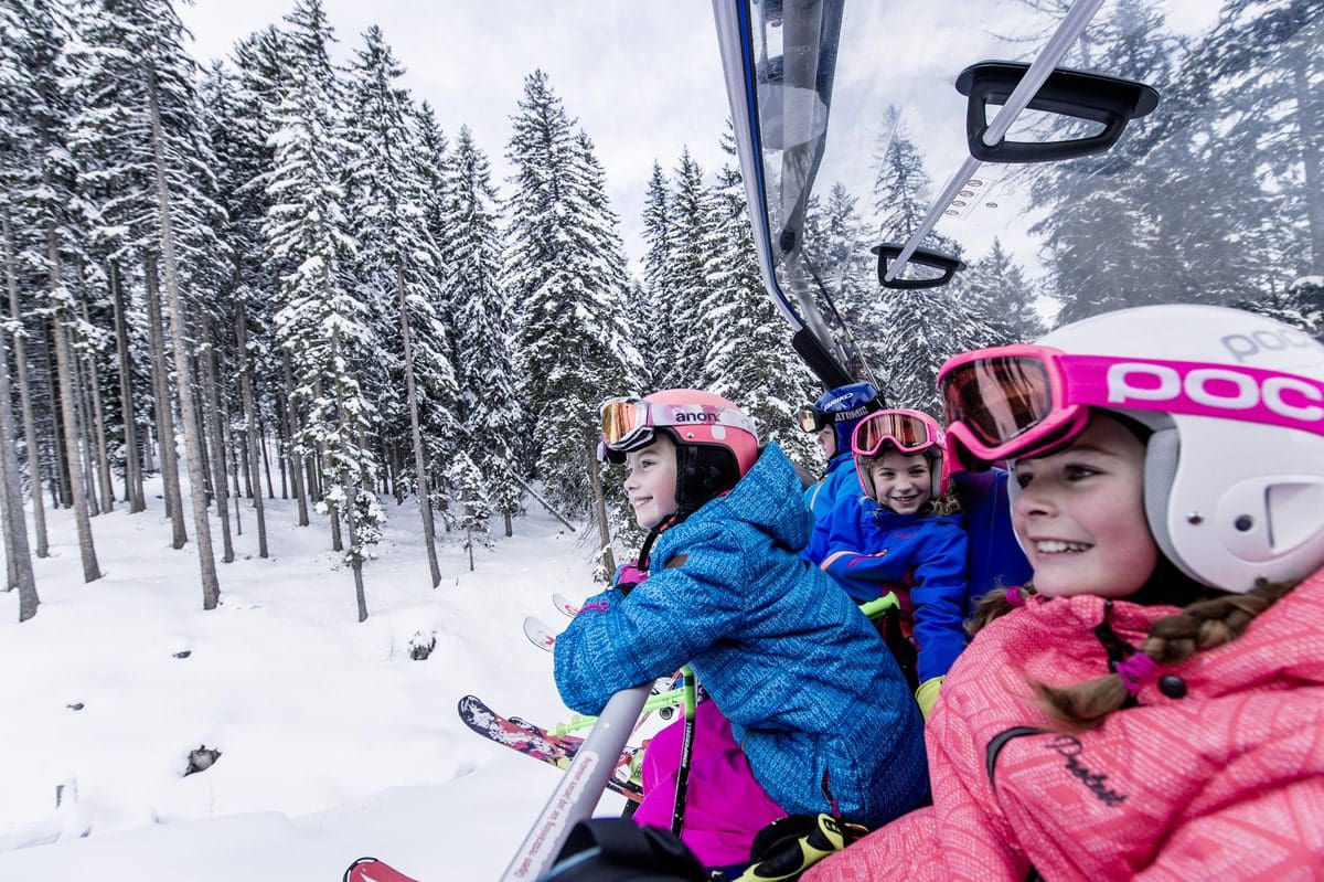 Kids smiling as they ride a gondola up the slopes to ski in Alpendorf.