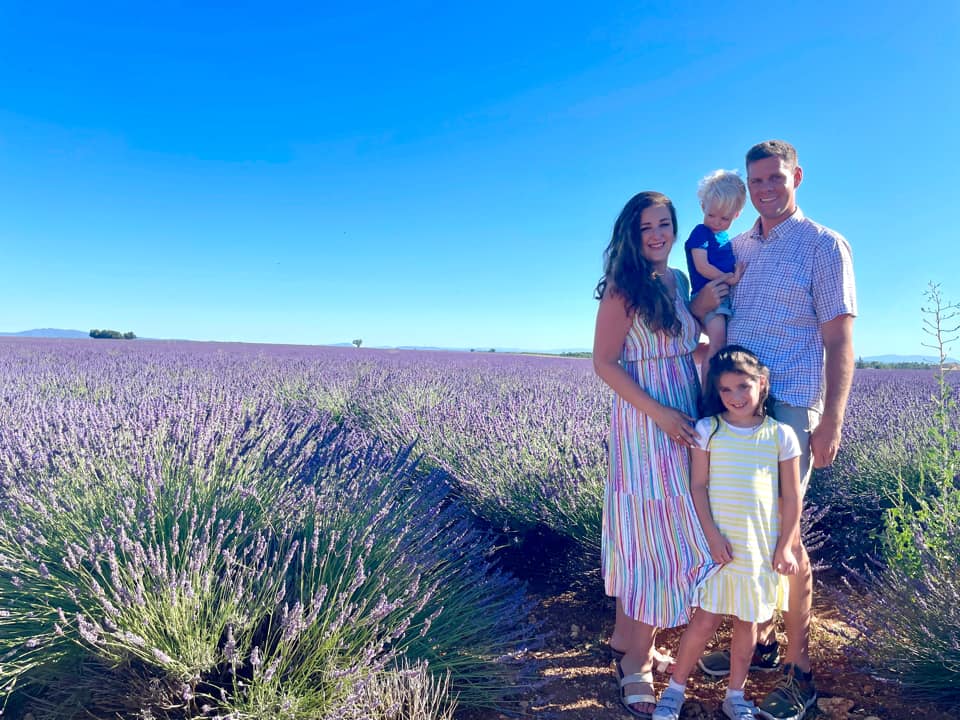 A family of four stands together smiling in a filed of French lavender in Valensole.
