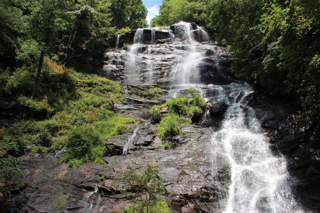A large waterfall cascades over carved rocks, flanked by lush greenery on both sides, in Amicalola State Park, one of the best family activities in North Georgia Mountains.
