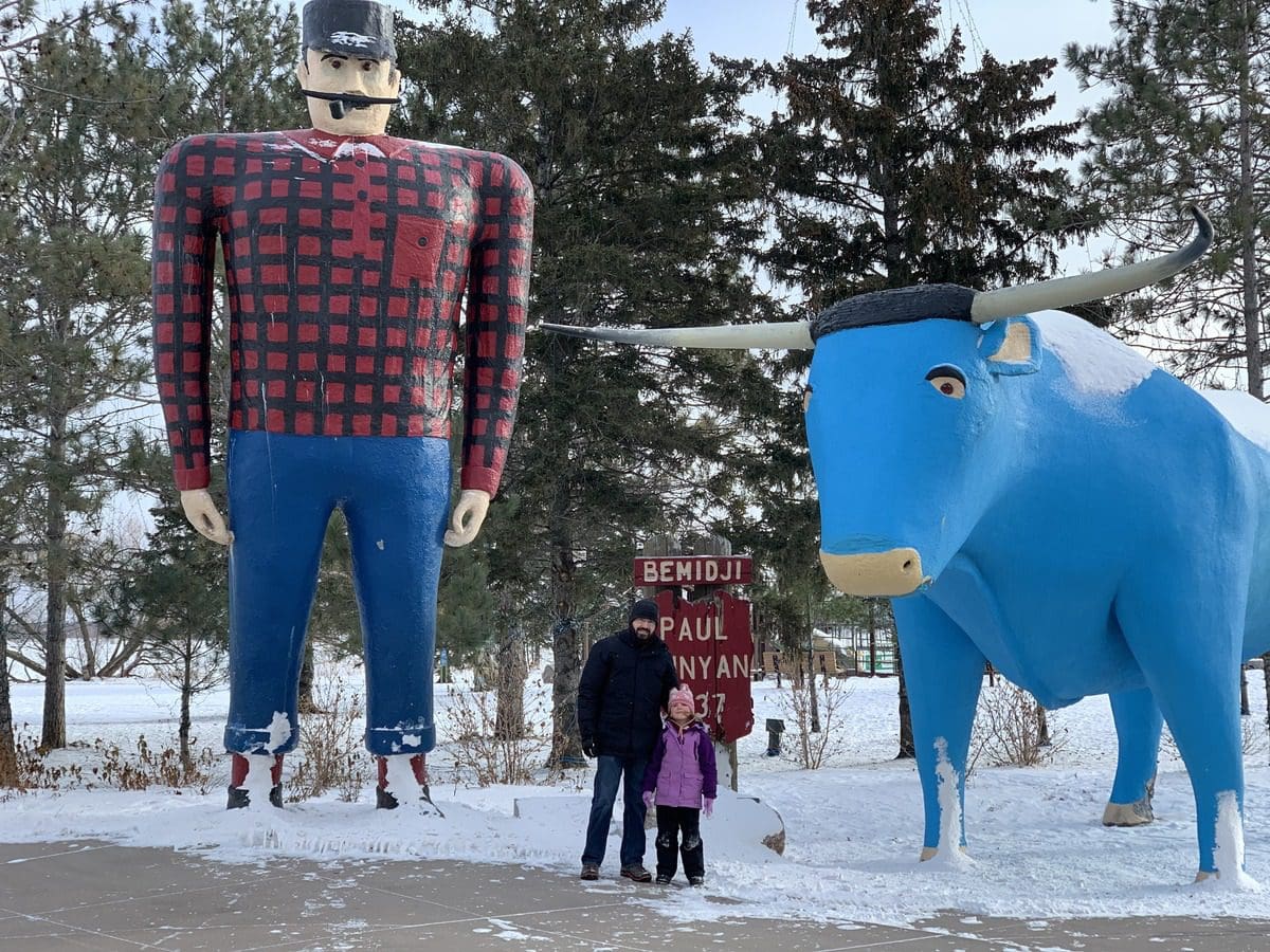 A dad and his young daughter pose near statues of Paul Bunyan and Babe the Blue Ox during winter in Bemidji.