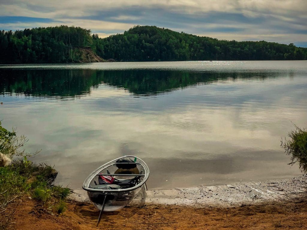 A clear bottom kayak rests along the shoreline of a pit mine lake in the Cuyuna area near Crosby, one of the best places to visit in northern Minnesota with kids.